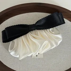 Détail de la pince à cheveux en satin plissé crème avec nœud noir sur plateau bois