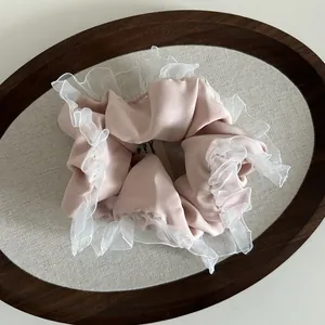 Detail of light pink satin scrunchie with white double-layer mesh ruffles on linen tray