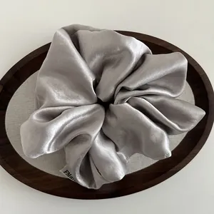 Close-up of a silver satin scrunchie with high glossy texture and a fabric label detail