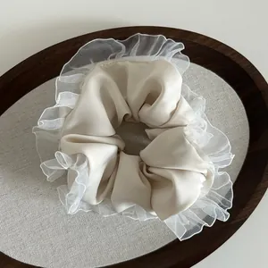 Detail view of cream satin scrunchie with delicate white lace trim on a wooden tray