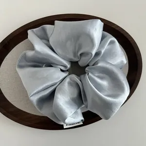 Detail of light blue satin oversized scrunchie with silky texture and woven label