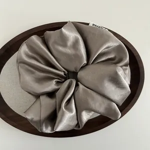 Detailed close-up of a large satin scrunchie in champagne gold on a wooden tray