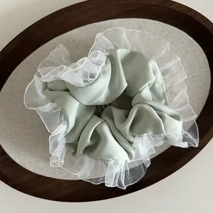 Detail of light green satin scrunchie with white organza ruffled edges on wooden tray