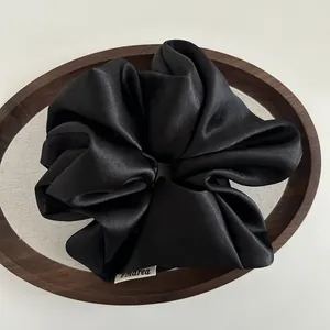 Macro view of a large black satin scrunchie with smooth silk-like texture and brand tag