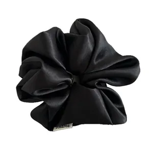 Large black satin scrunchie with glossy finish and brand label for high ponytail