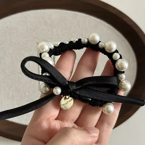 Dettaglio di un elegante elastico in raso nero con perle bianche e ciondolo fatto a mano