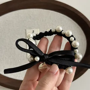 Dettaglio di elegante elastico per capelli con fiocco, perle nere e ciondolo dorato