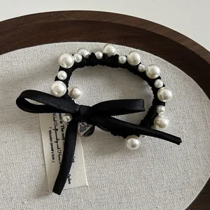 Dettaglio di elegante elastico per capelli con fiocco nero, perline bianche e ciondolo