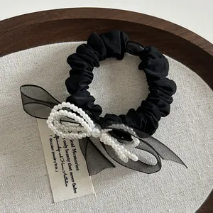 Dettaglio dell'elegante scrunchie in seta nera con decorazione di fiocco in tulle e perle