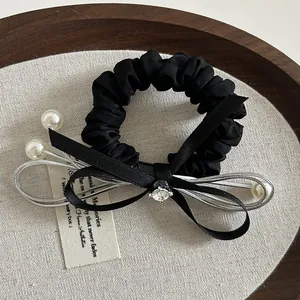 Dettaglio dello scrunchie in raso nero con fiocco di perle e centro in strass