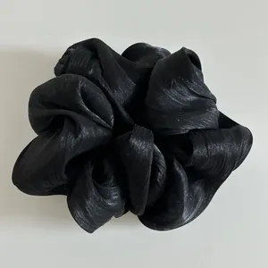 Λεπτομέρεια μαύρου σατέν scrunchie με πλισέ υφή και μεταξένια γυαλιστερή εμφάνιση