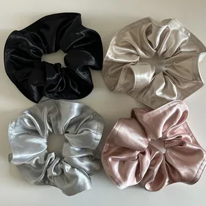 Dettaglio di quattro elastici scrunchie in raso lucido nei colori nero, oro e rosa