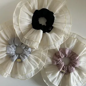 Detailed view of oversized chiffon scrunchies in black, gray and pink with golden labels