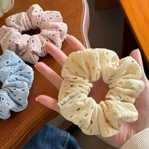 Detailed close-up of three floral eyelet fabric scrunchies in pastel pink, blue and beige