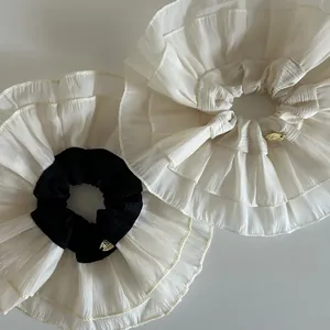 Close-up of double-layered lace scrunchies with elegant gold metal logo tag detail