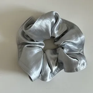 Vista dettagliata dell'elastico scrunchie in raso grigio argento con tessuto lucido e cuciture