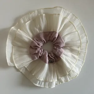 Detail of oversized layered scrunchie with beige ruffles and pink center with silver label
