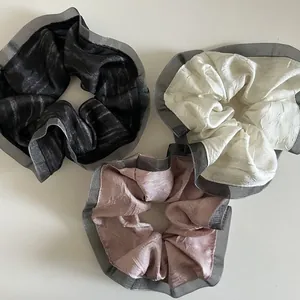 Detailed view of three pleated fabric hair scrunchies in black, beige and dusty pink