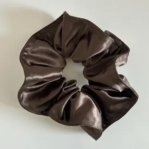 Dettaglio di un elastico per capelli in raso marrone scuro lucido e setoso