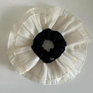 Detail of oversized double-layer lace scrunchie with pleated chiffon and metal logo tag