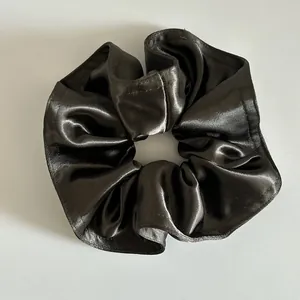 Vista dettagliata dello scrunchie in raso grigio scuro con texture lucida e pieghe