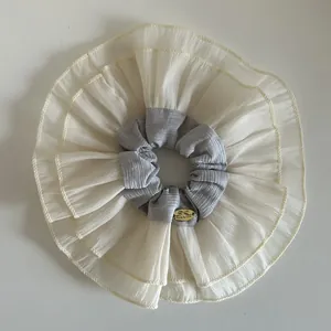 Close-up of oversized layered ruffle scrunchie with gold logo tag and soft mesh texture
