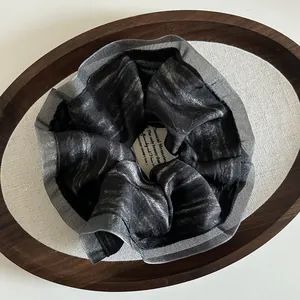 Detail of elegant black metallic pleated hair scrunchie in a wooden display tray