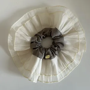 Detail of multi-layered lace scrunchie with grey fabric and golden metal label