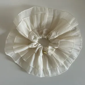 Close-up of cream-colored ruffled hair scrunchie with layered design and gold emblem