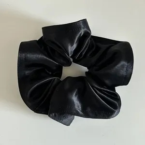 Dettaglio di un elastico per capelli in raso nero con texture a pieghe e finitura lucida