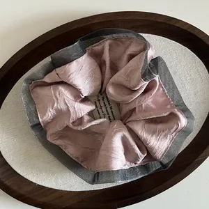 Detail of pink satin scrunchie with grey mesh lace trim in an oval wooden tray