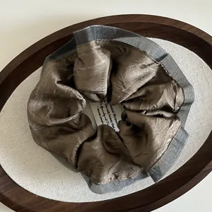 Close-up of silk-textured dark brown scrunchie with layered grey mesh lace trim