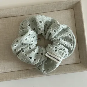 Detail of mint green eyelet fabric scrunchie with a Happy Every Day woven label