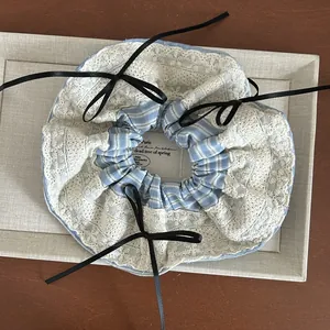 Detail of blue striped scrunchie with white lace trim and black ribbon bows on a tray