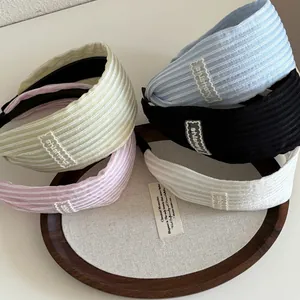 Cinq serre-têtes en tissu rayé aux couleurs pastel présentés sur un plateau en bois