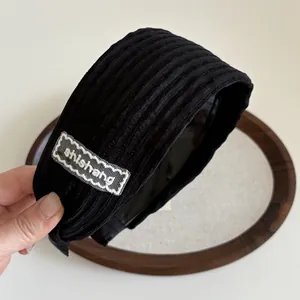 Détail d'un serre-tête large noir texturé avec patch en dentelle blanche brodée