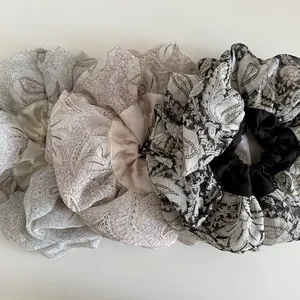 Detailed view of three oversized floral scrunchies in paisley satin and chiffon fabric