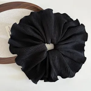 Detailed close-up of large black pleated fabric hair scrunchie with elegant wavy edges