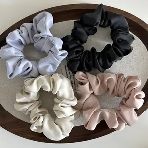 Set de cuatro coleteros de satén brillante en morado, negro, blanco y rosa en bandeja madera