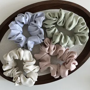 Detalle de textura de cuatro coleteros de satén en colores Morandi en bandeja de madera