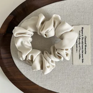 Detalle de un coletero de satén beige crema con textura de seda en una bandeja de madera