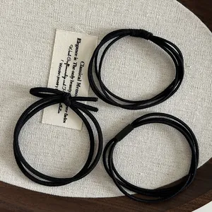 Close-up of black elastic hair ties set with bow detail on rustic linen background