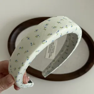 Nahaufnahme des gepolsterten Blumenstirnbandes mit blau-grünen Blüten auf Beige