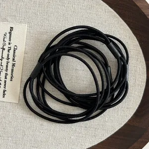 Close-up of high-elasticity black hair ties with reinforced joints on a rustic tray