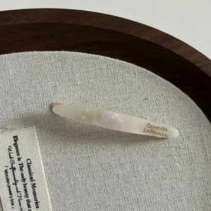 Détail de la barrette en acétate crème avec effet nacré et texte doré élégant