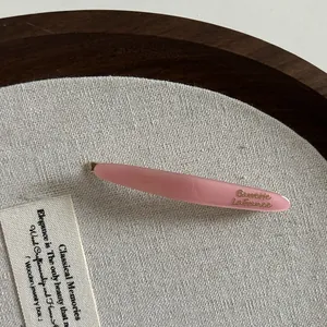 Détail macro d'une barrette en acétate rose avec lettrage doré sur support en toile