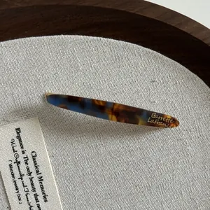Détail macro d'une barrette en acétate avec motif écaille bleue et logo doré élégant