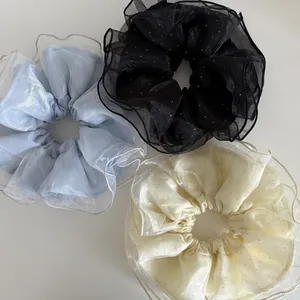 Détail de trois chouchous en organza double couche noir, bleu clair et beige à pois argentés