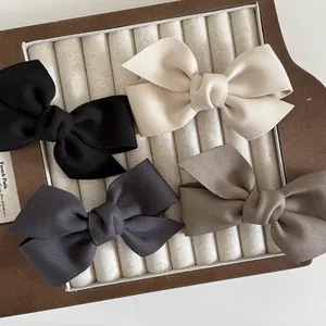 Dettaglio di quattro fermagli per capelli in raso nei toni nero, beige, grigio e marrone