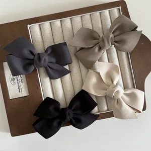 Dettaglio di quattro fermagli per capelli a fiocco in raso grigio, kaki, beige e nero